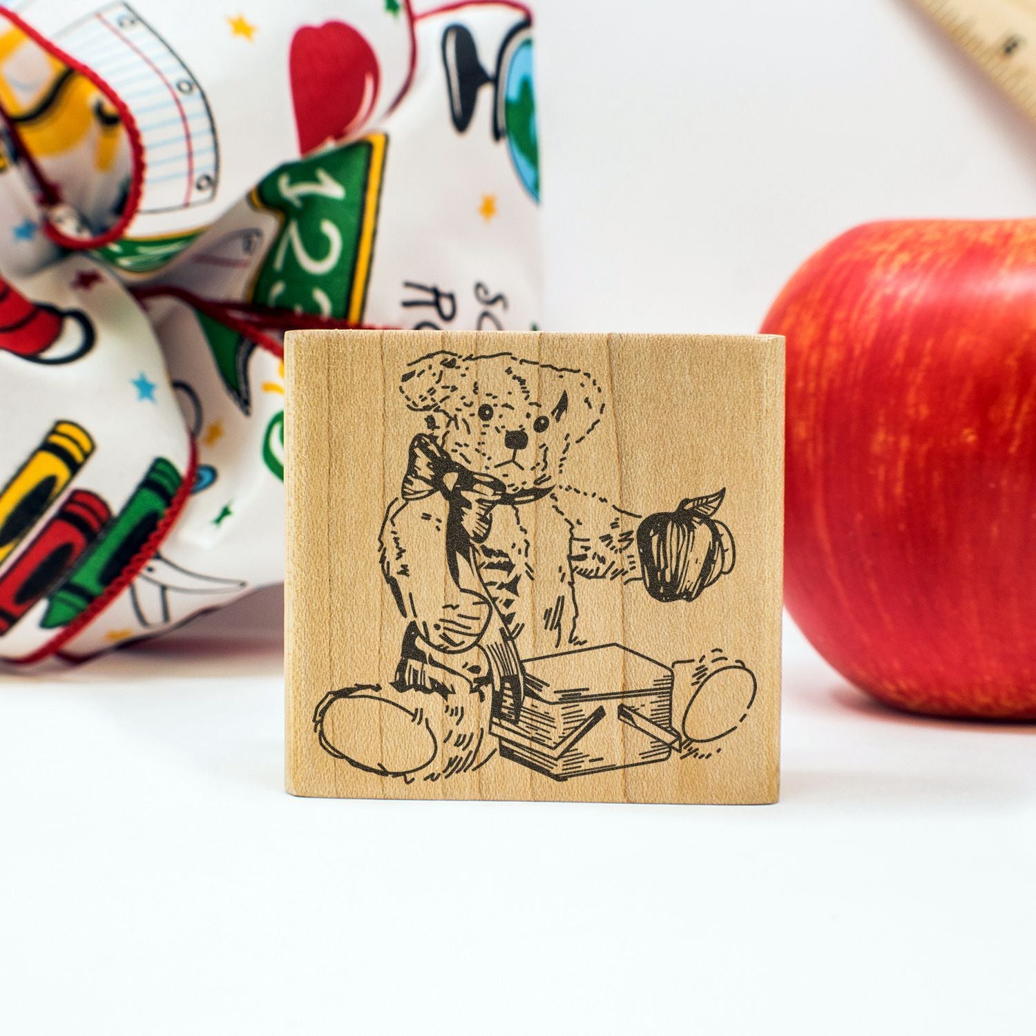 Wooden teddy bear stamp with apple and colorful school supplies in the background