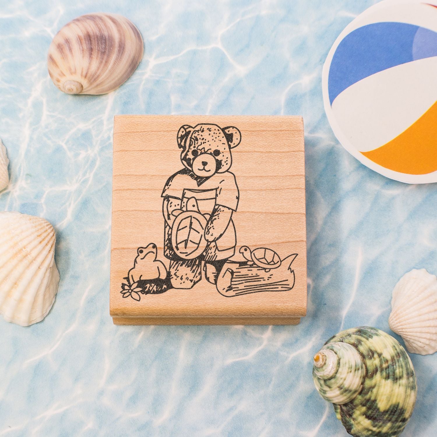 Wooden beach-themed stamp with bear, turtle, and frog illustration surrounded by seashells and a colorful beach ball on a blue ocean background