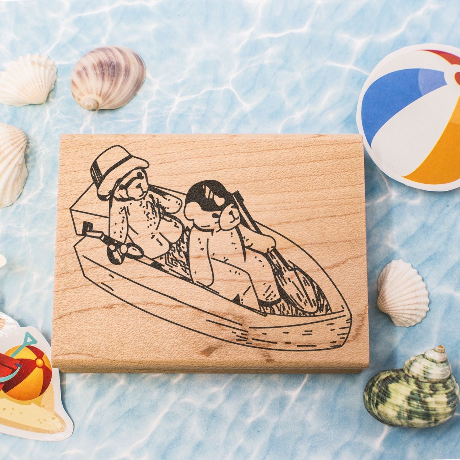 Wooden stamp with two dogs in a boat, surrounded by seashells and beach toys on a summer beach-themed background