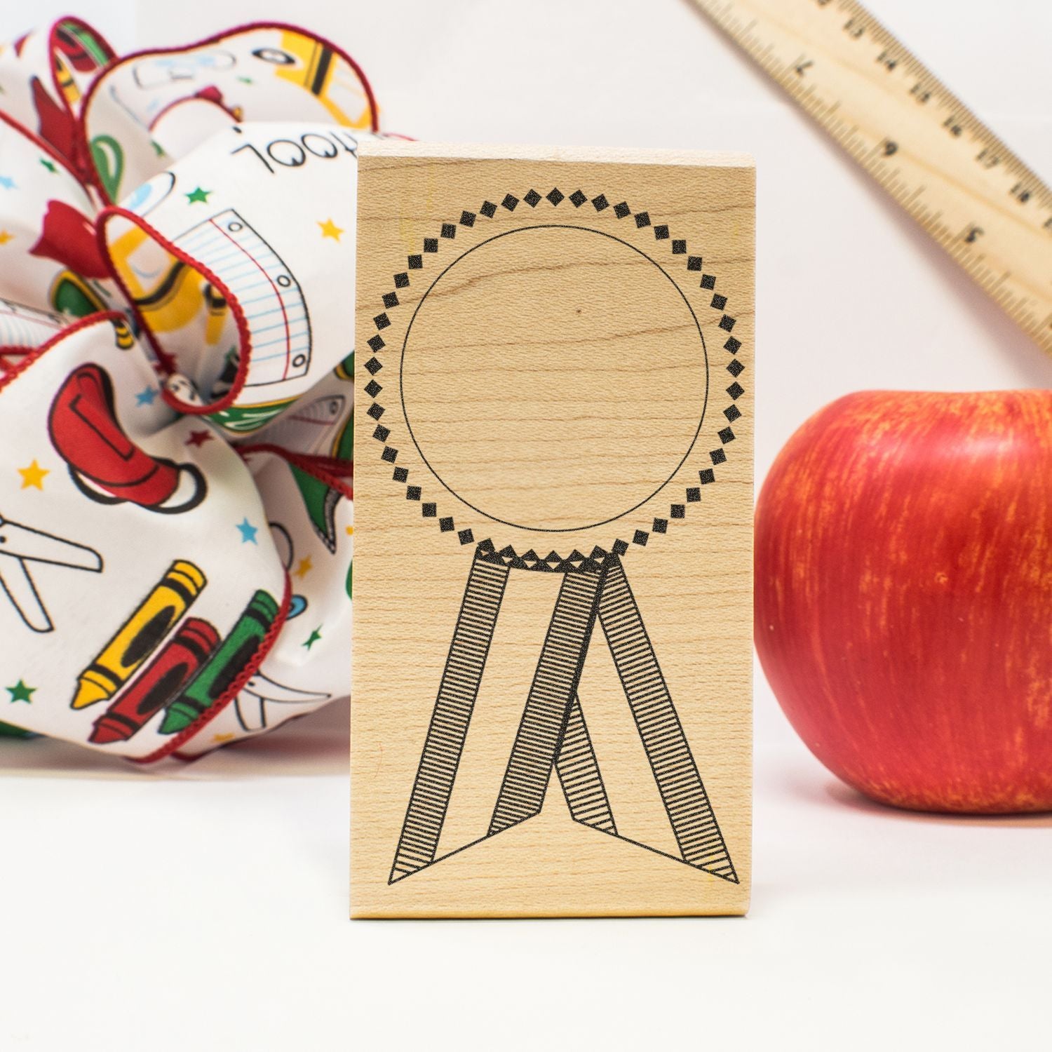 Wooden award ribbon stamp with apple, ruler, and school craft supplies on white background