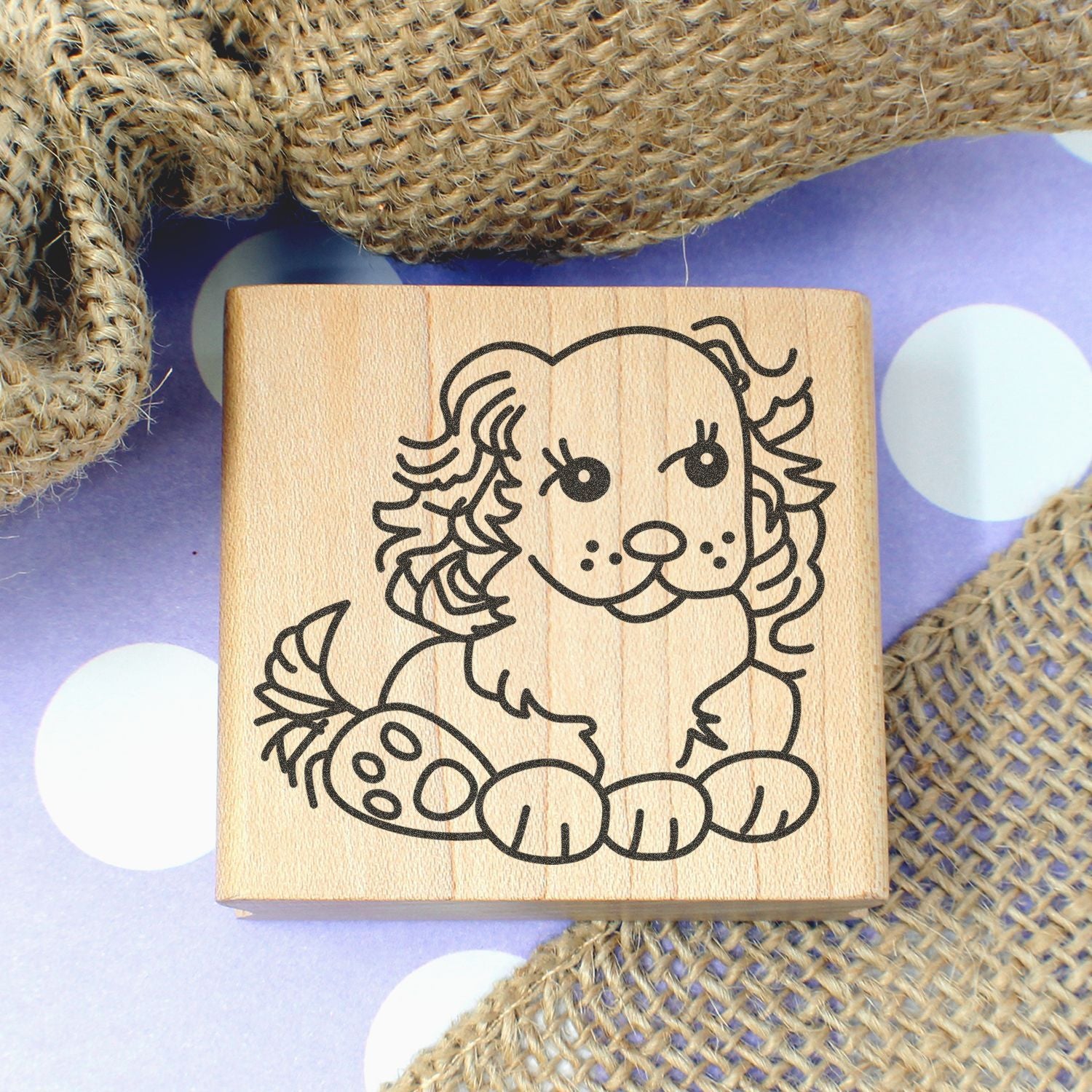 Cute dog wooden stamp with puppy illustration on a purple polka dot background, surrounded by burlap fabric.