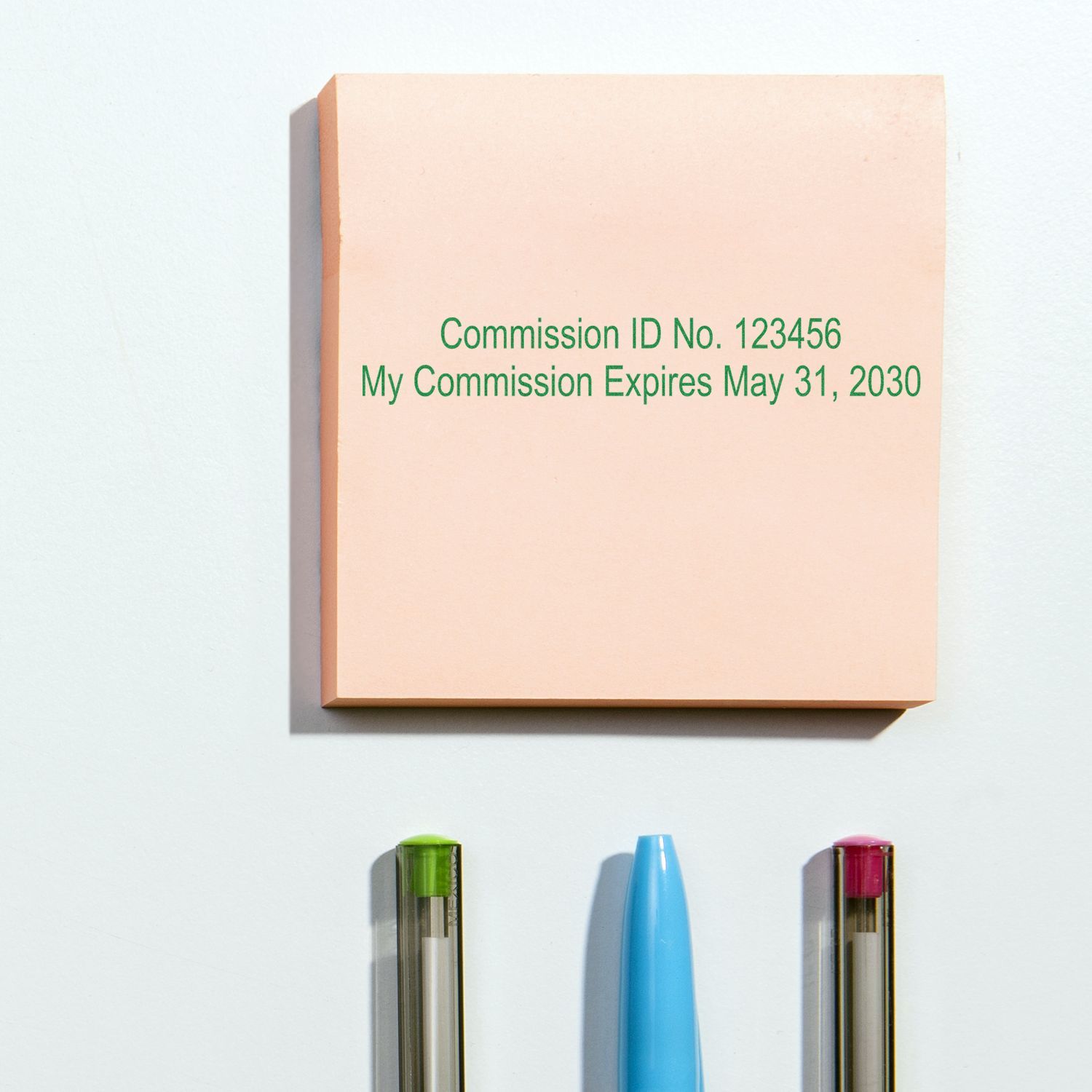 Notary commission ID plaque with expiration date and pens on a white wall.