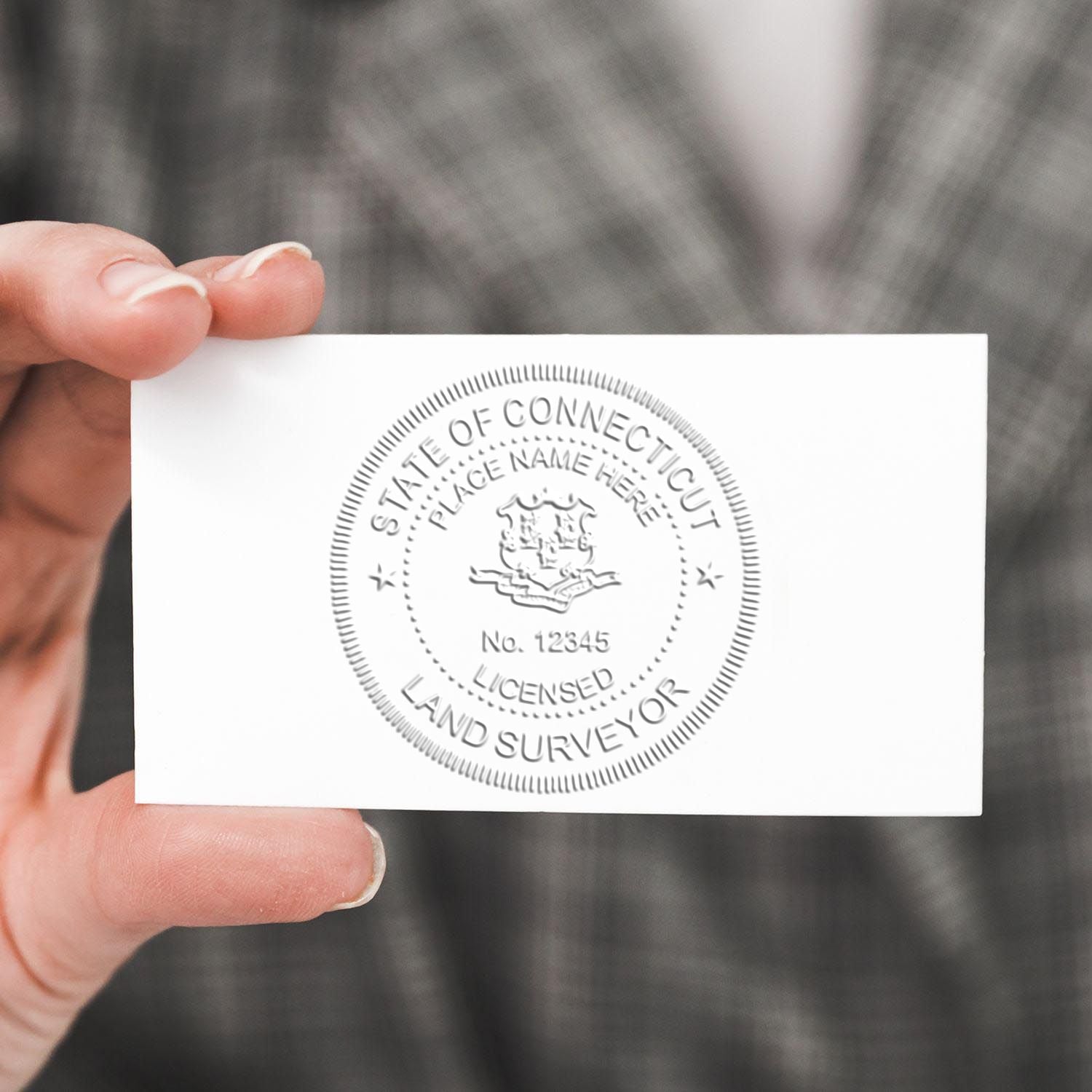 Hand holding a State of Connecticut licensed land surveyor embossed business card seal.