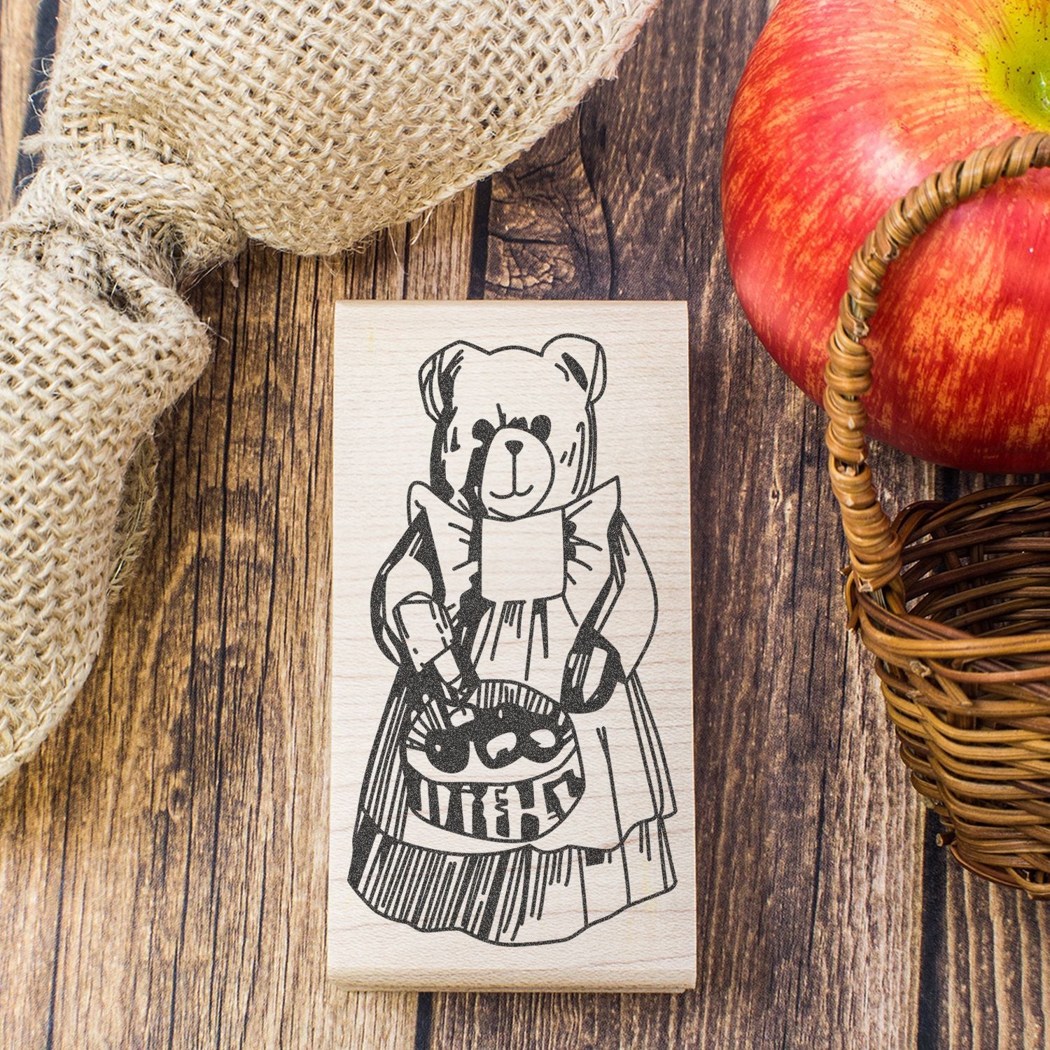 Halloween teddy bear rubber stamp with trick-or-treat bag on rustic wooden table beside burlap and apples.