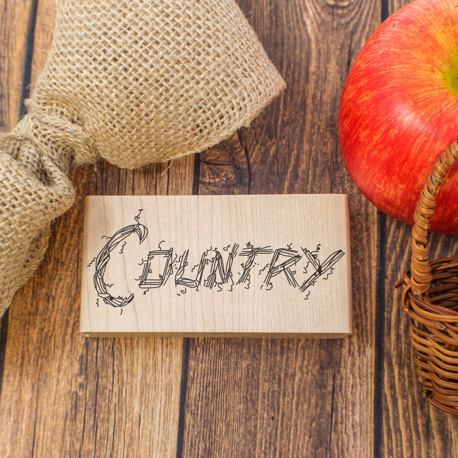 Rustic bakery-themed wooden stamp with burlap and red apple on a wooden table.