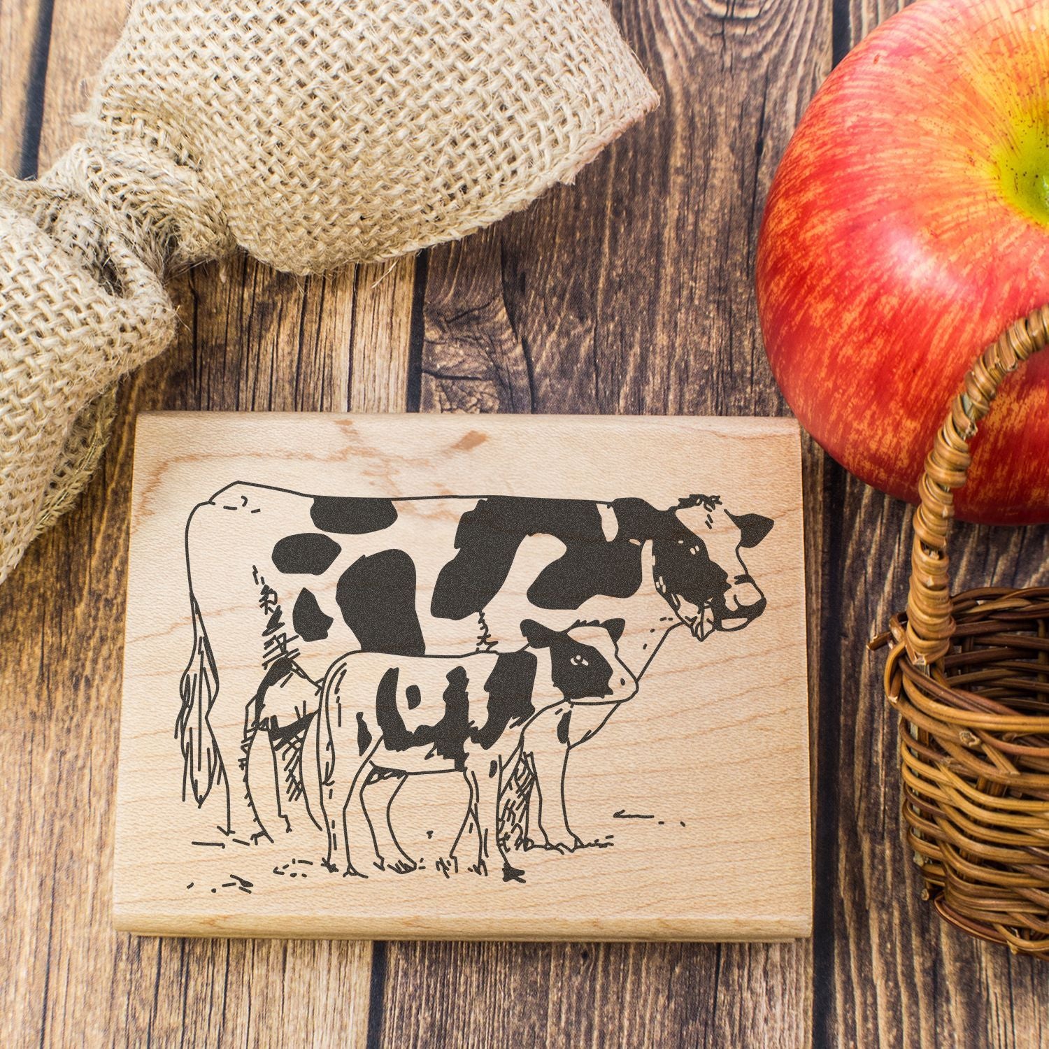 Rustic farmhouse wooden plaque with cow and calf illustration, autumn apple decor, and burlap accents on a wooden table.