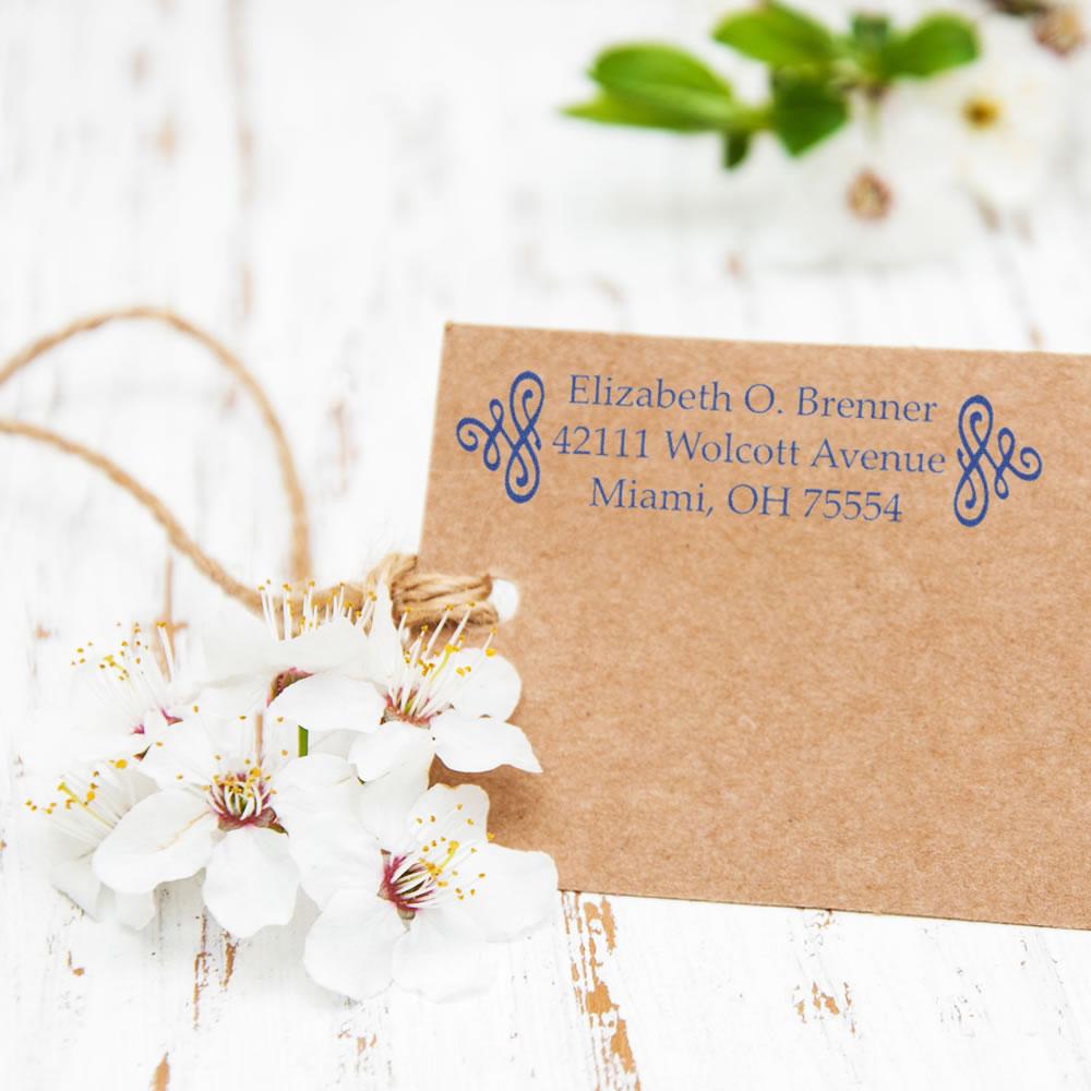 Custom return address rubber stamp on kraft envelope with blue monogram, ideal for wedding invitations and business mail.