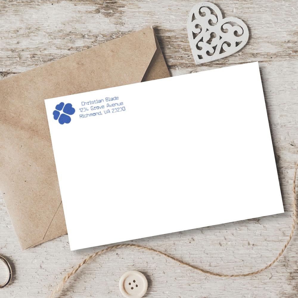 Personalized return address rubber stamp on stationery, with blue logo imprint on a white card beside a kraft envelope.