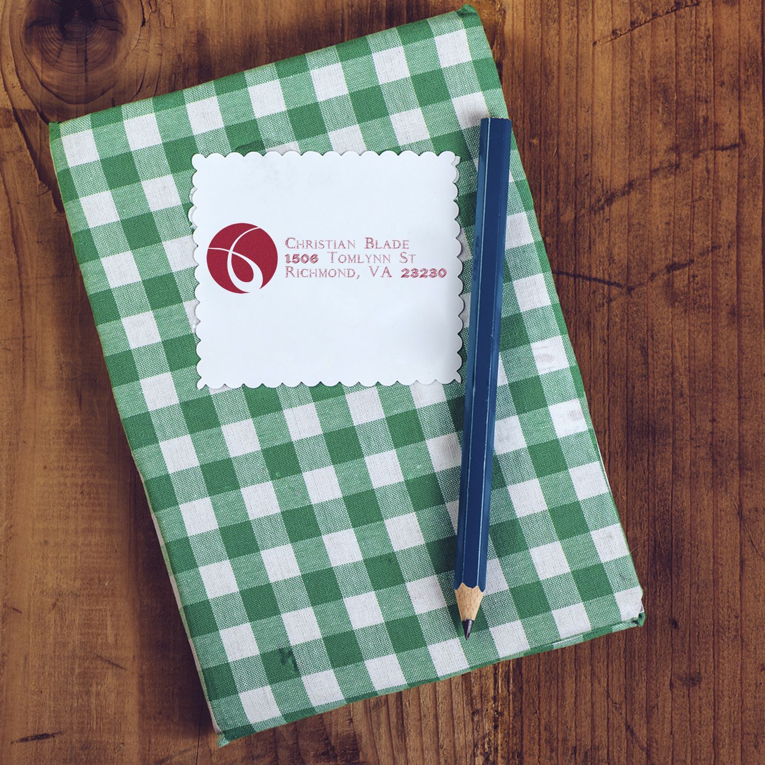 Custom return address rubber stamp on a scalloped note card, shown with a green notebook and pencil.