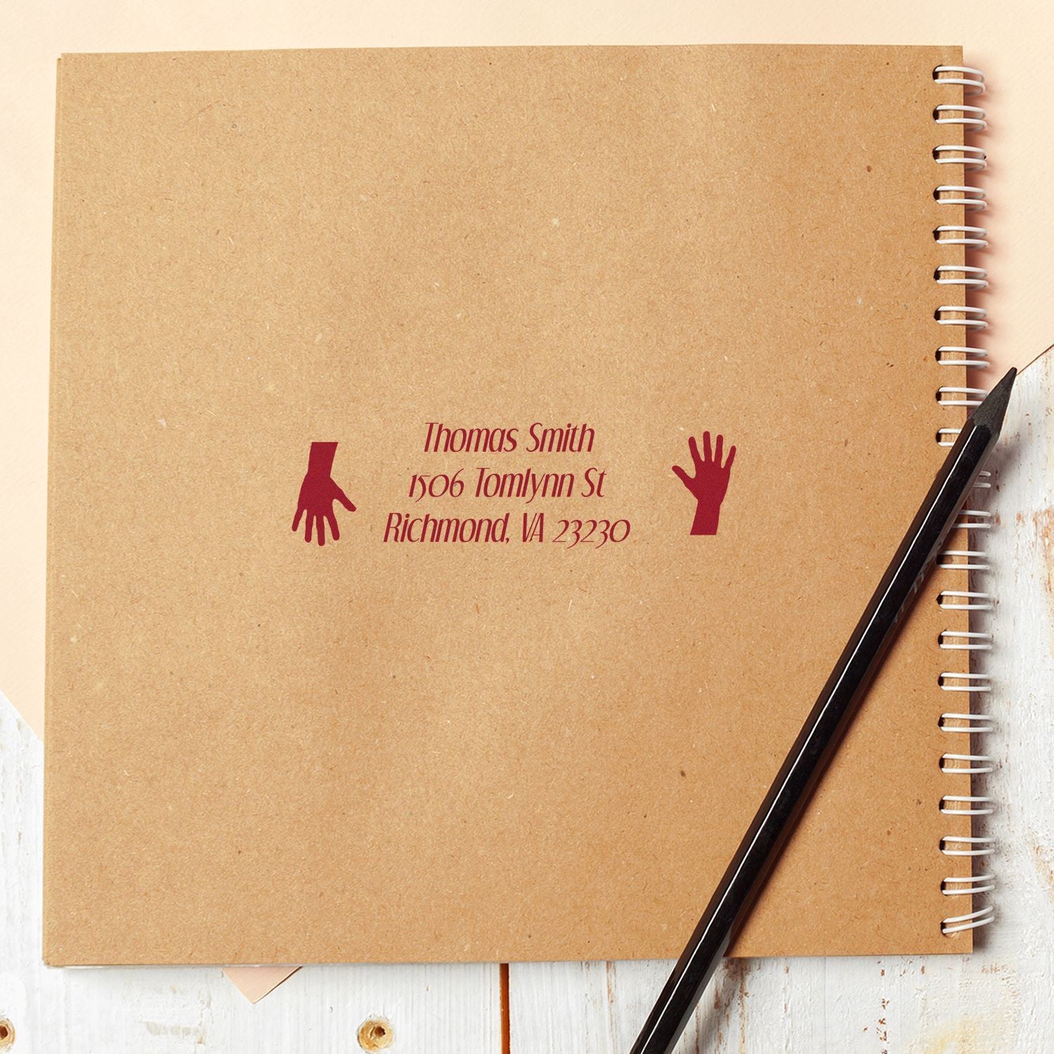 Custom return address rubber stamp with name, address and hand icons on kraft notebook.