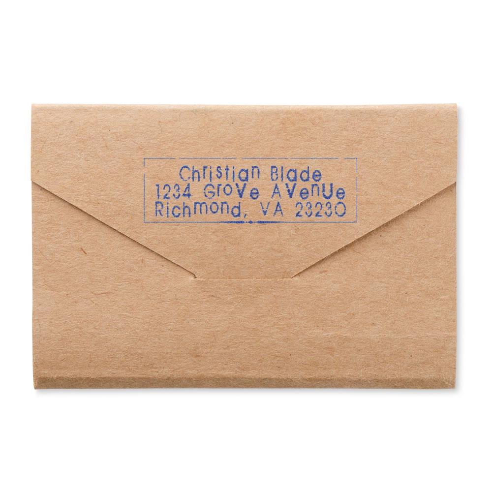 Custom address rubber stamp on kraft envelope with blue ink, featuring name and mailing address for business or personal mail.