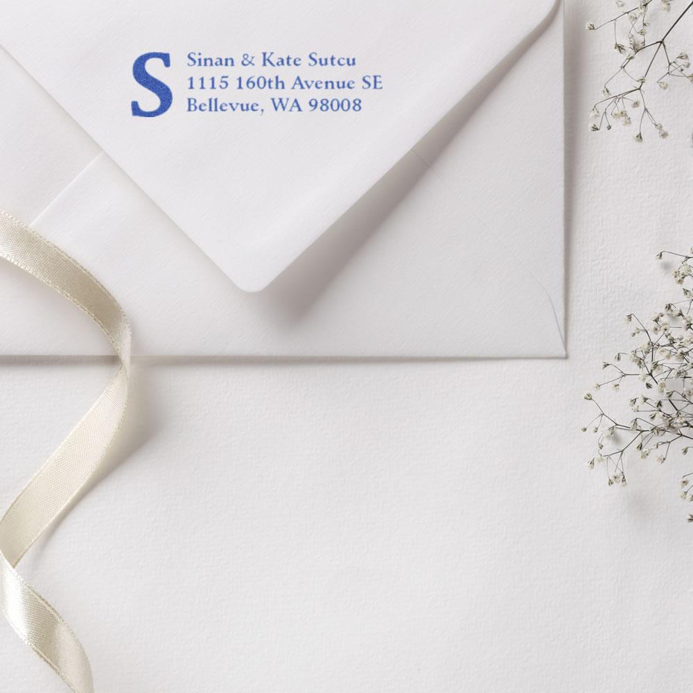 Personalized return address rubber stamp on wedding envelope with monogram initial S, blue ink.