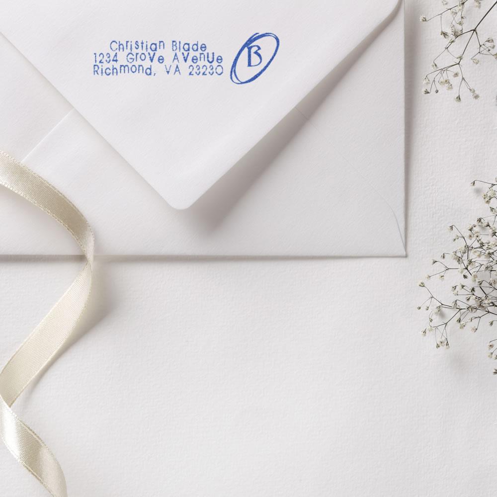 Custom return address rubber stamp on white wedding invitation envelope with blue monogram and address.