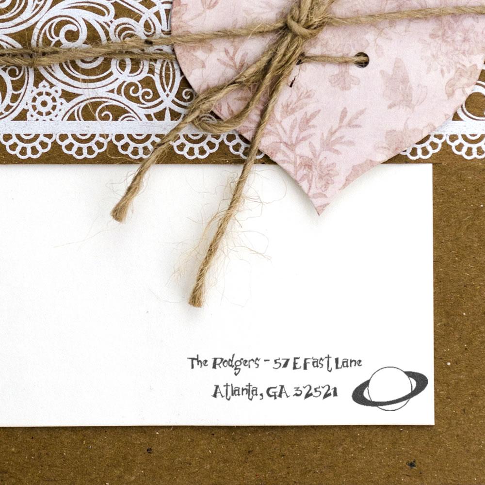 Personalized return address rubber stamp on rustic wedding invitation envelope with twine and lace accents.