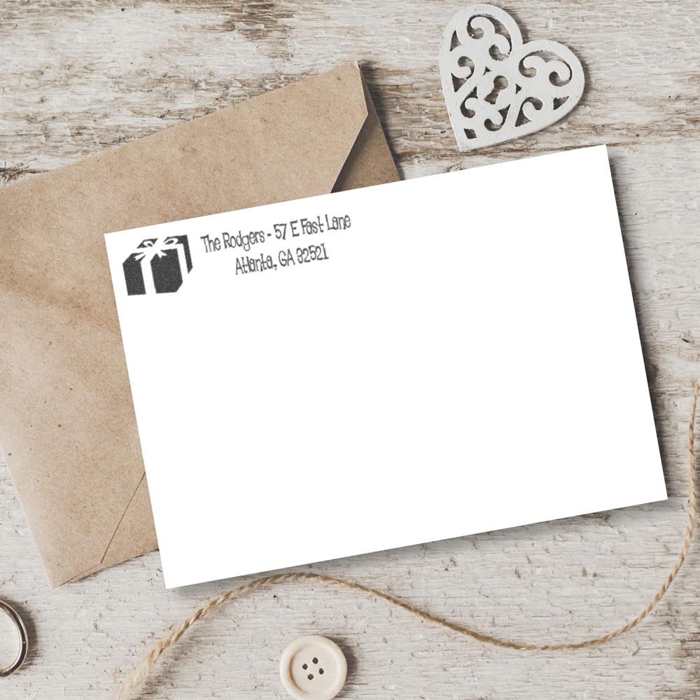 Custom address rubber stamp on envelope and card with gift icon, ideal for invitations, packaging, and business mailings.