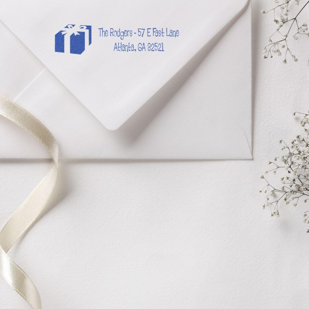 Custom return address rubber stamp on white envelope with gift icon and blue address print