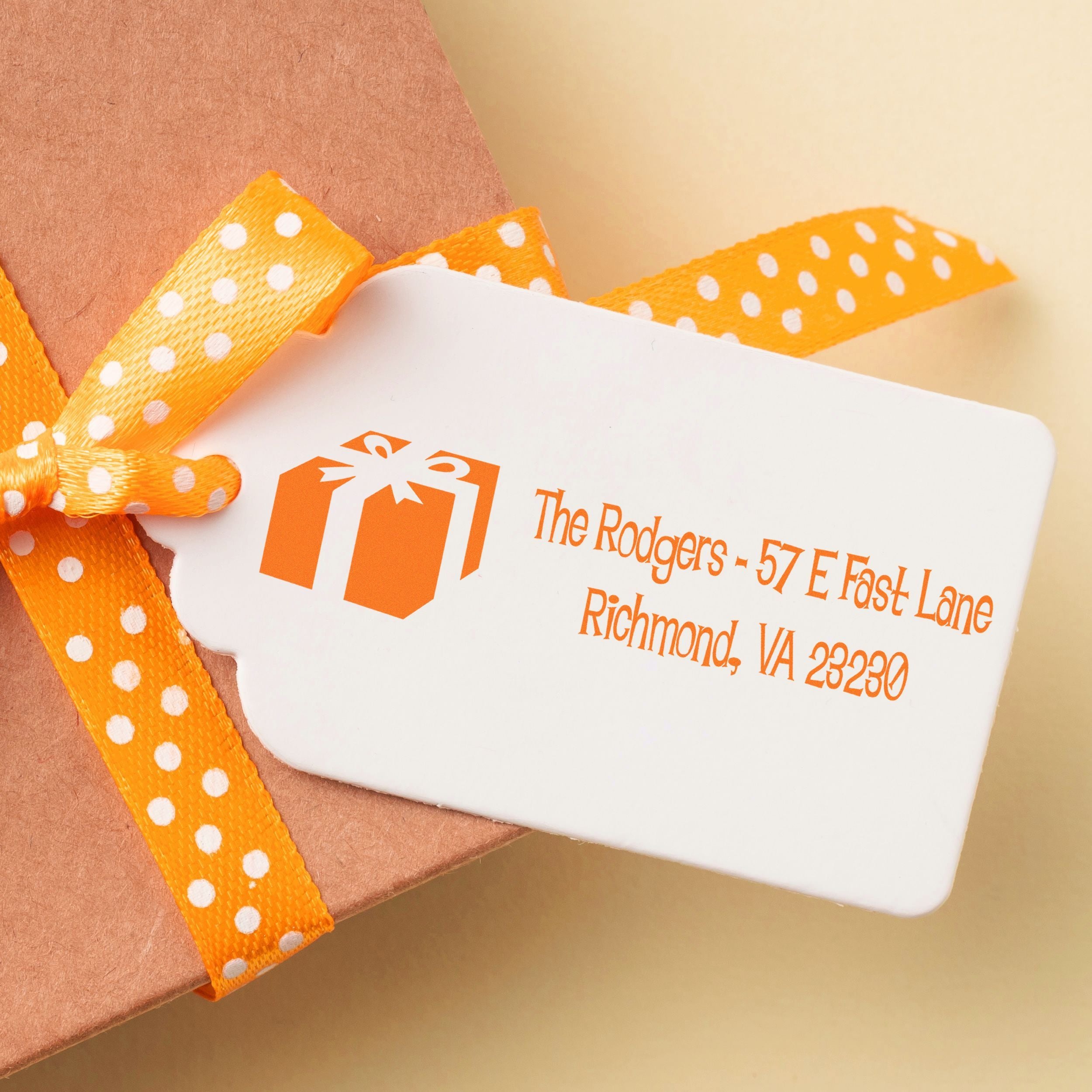 Custom return address rubber stamp on gift packaging with orange polka dot ribbon for personalized branding.