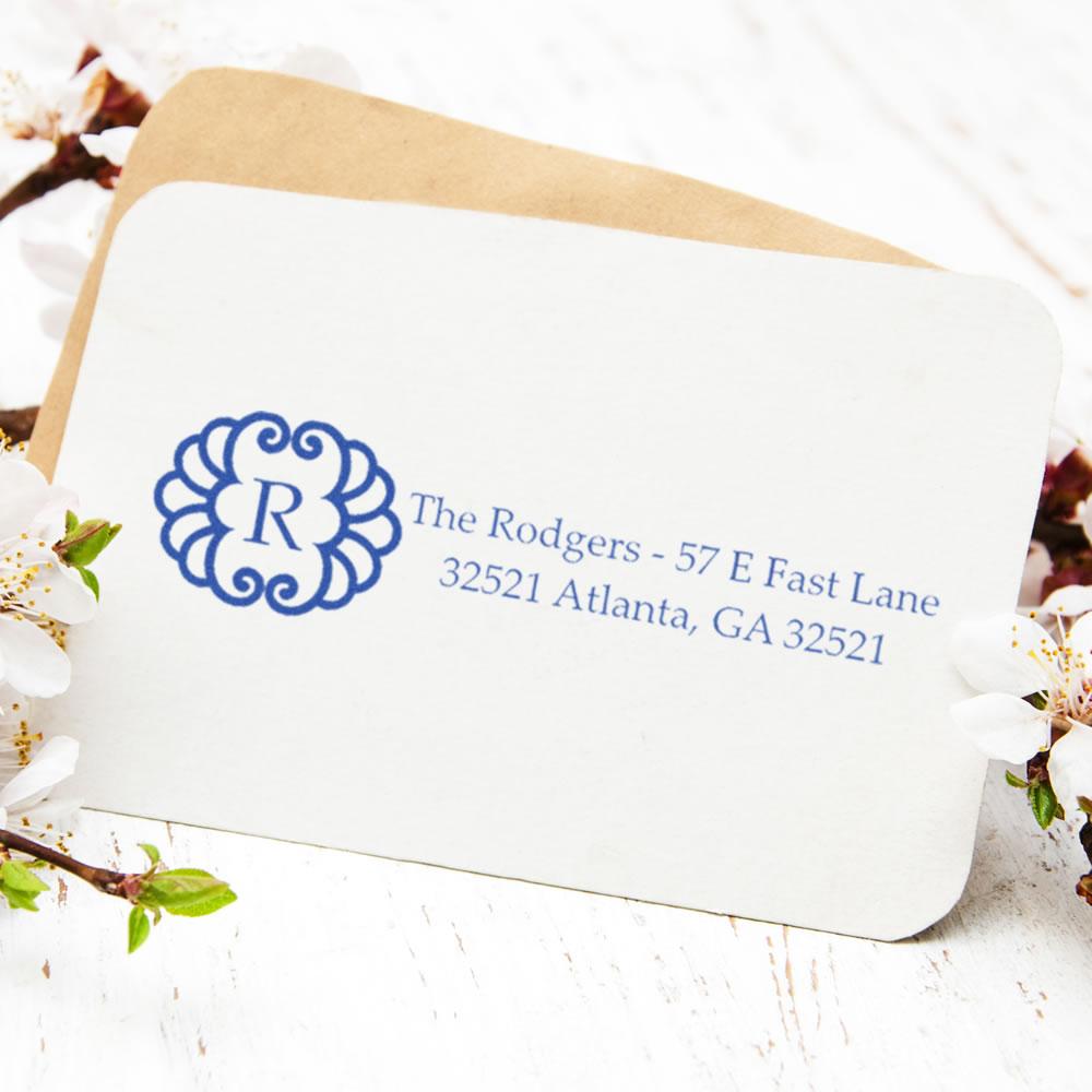 Custom monogram return address rubber stamp on envelope with blue floral initial and personalized family address.