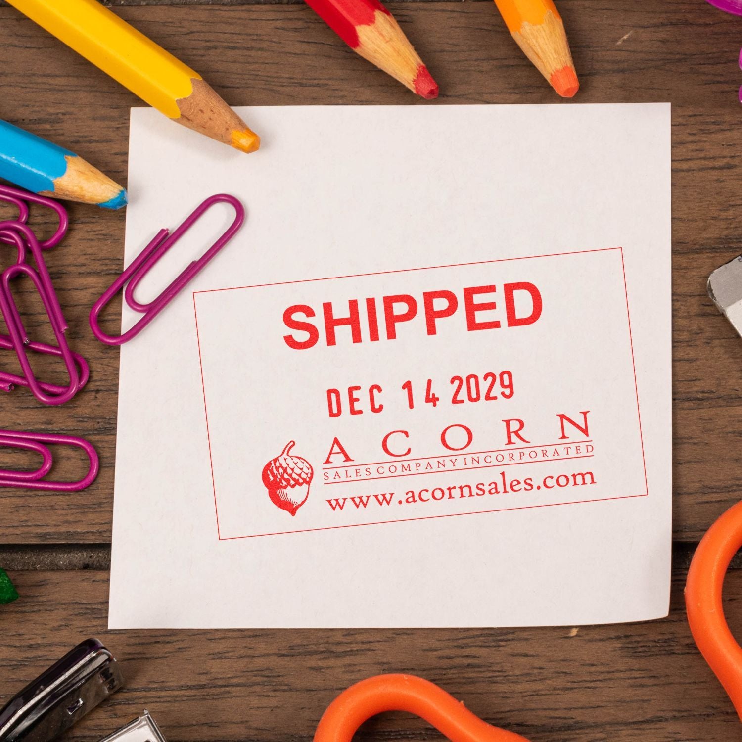 Shipped stamp on white paper with colorful pencils and paper clips on a wooden desk, featuring Acorn Sales branding.