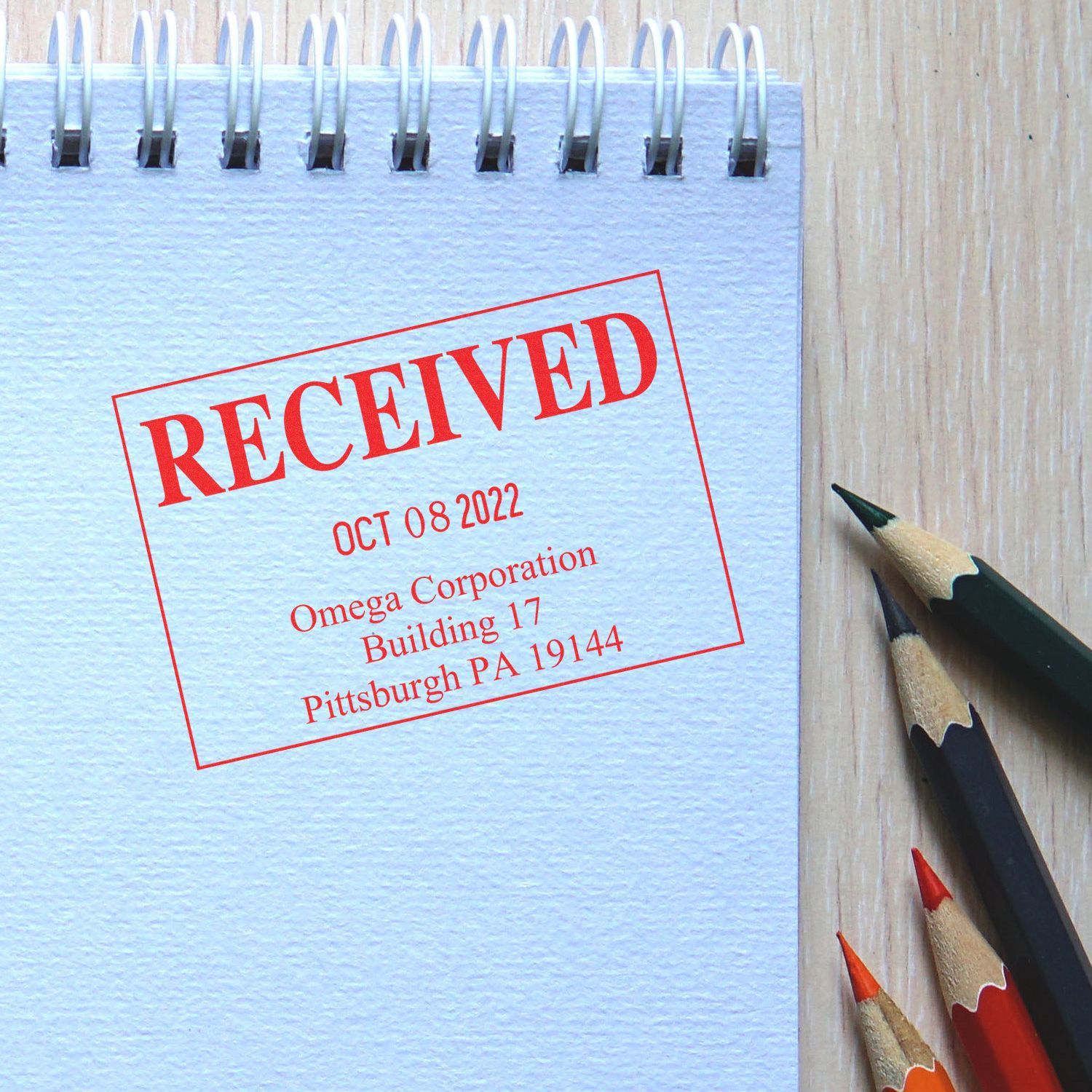 Notebook page with red RECEIVED stamp on wooden desk beside colored pencils, business document approval concept.