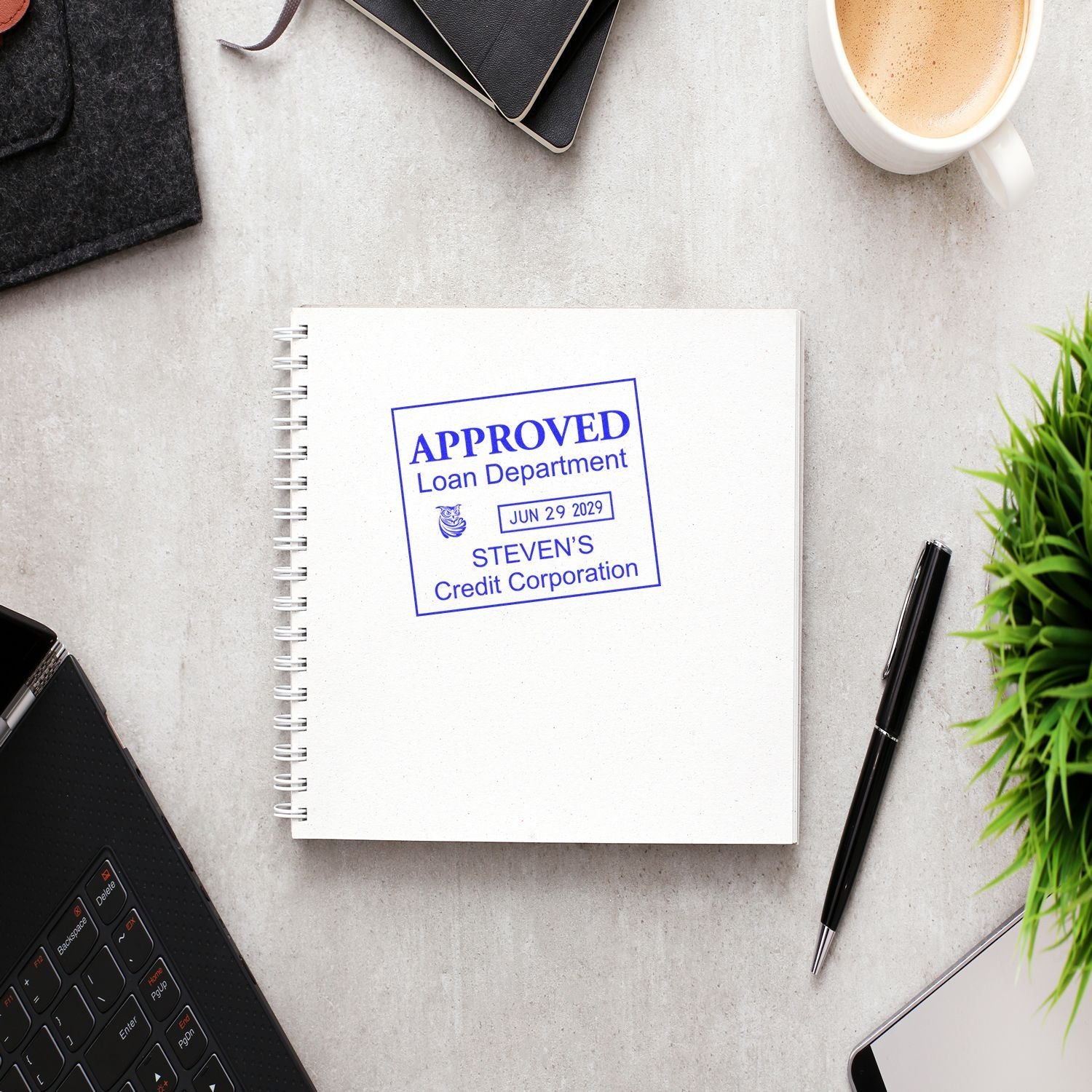 Approved loan department stamp on notebook with office desk items, laptop, coffee cup, pen, and plant, representing credit approval and business finance.