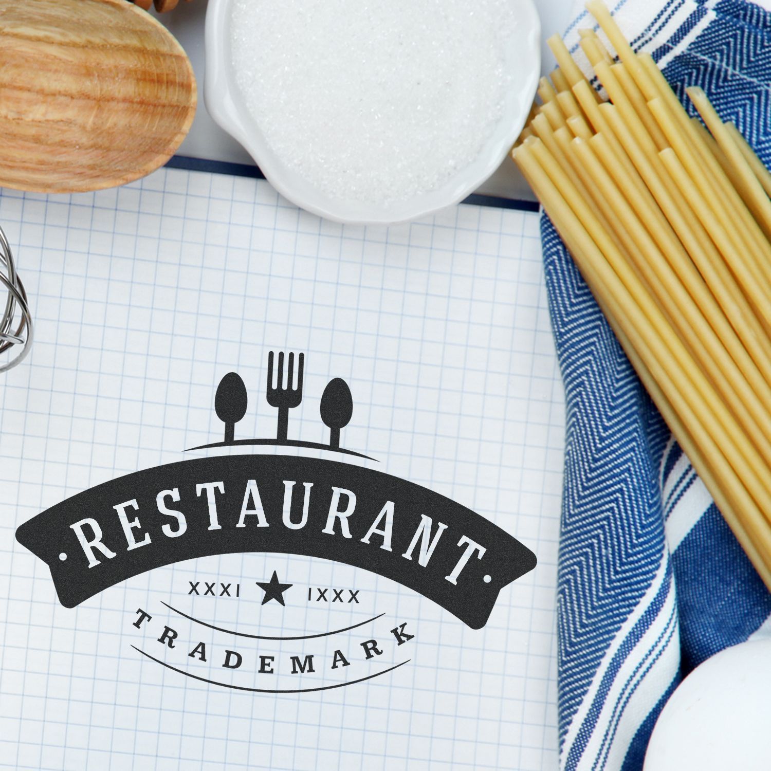 Restaurant marketing flat lay with restaurant emblem and cutlery icons, bowl of salt or sugar, wooden board and Italian spaghetti on lined notebook paper.