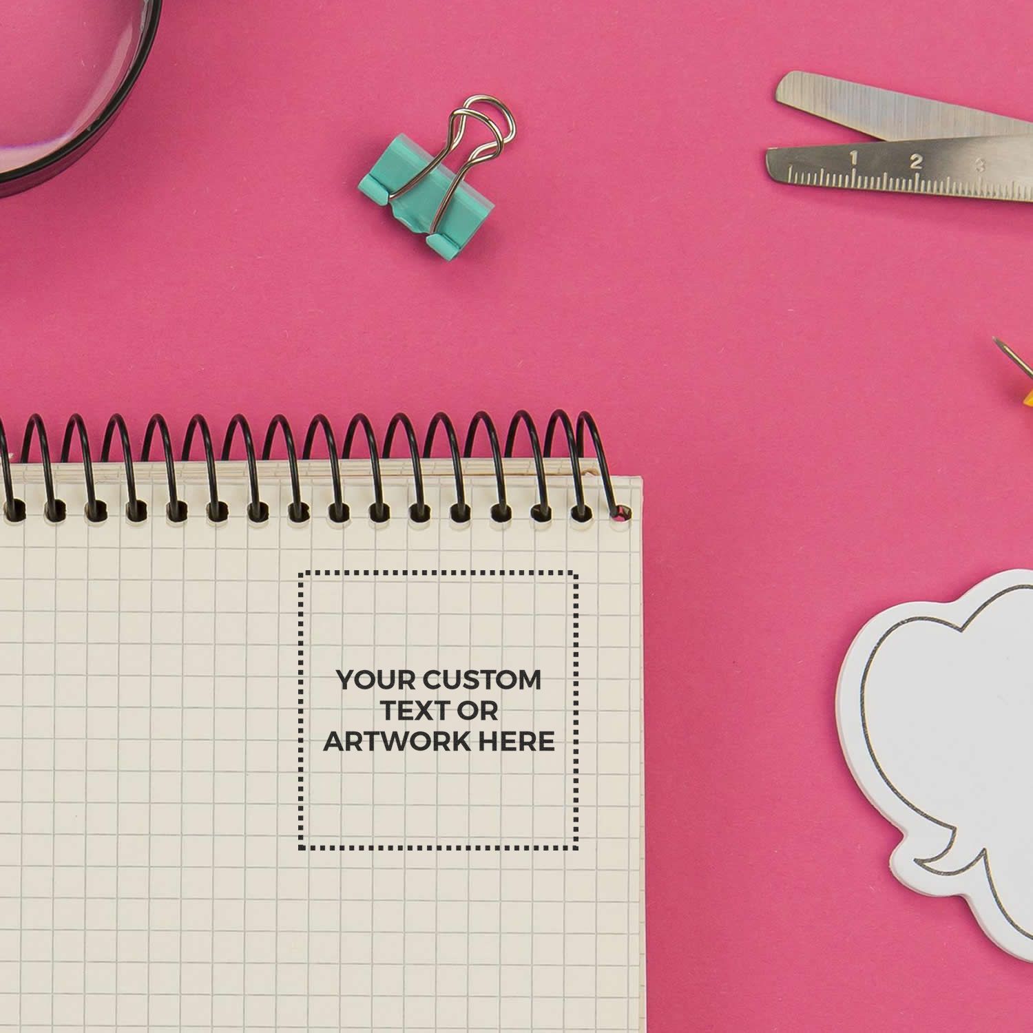 Pink stationery flat lay with spiral notebook, binder clip, ruler, and blank custom text template on a bright background.