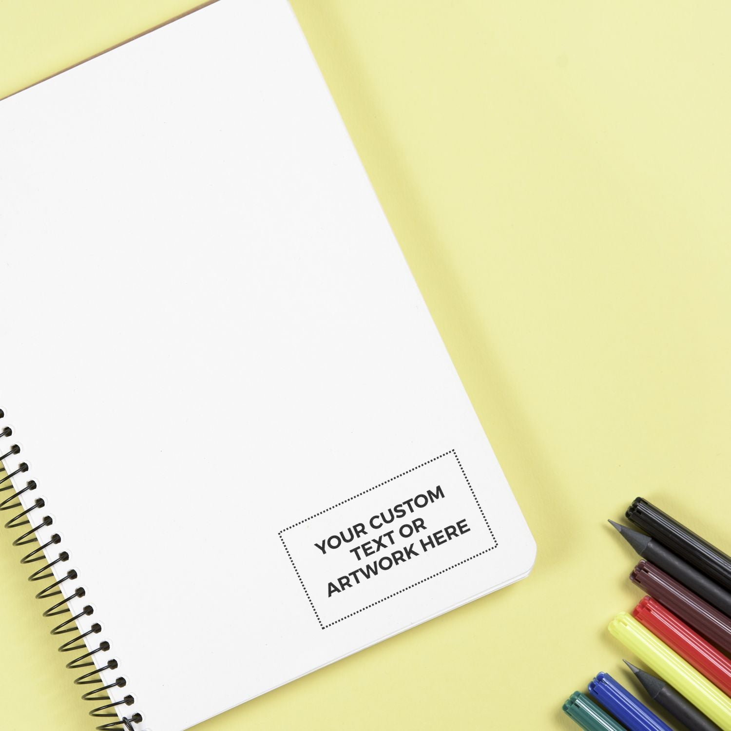 Blank spiral notebook mockup with custom text placeholder, colorful pens, and yellow background for branding or design presentation