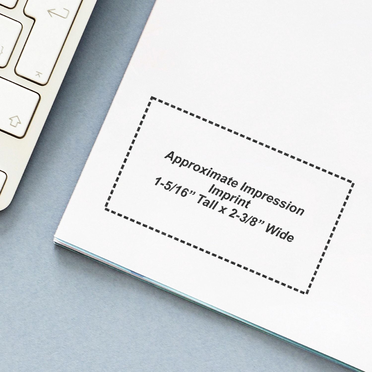 Printed design template showing approximate impression imprint size next to a laptop keyboard on a desk.