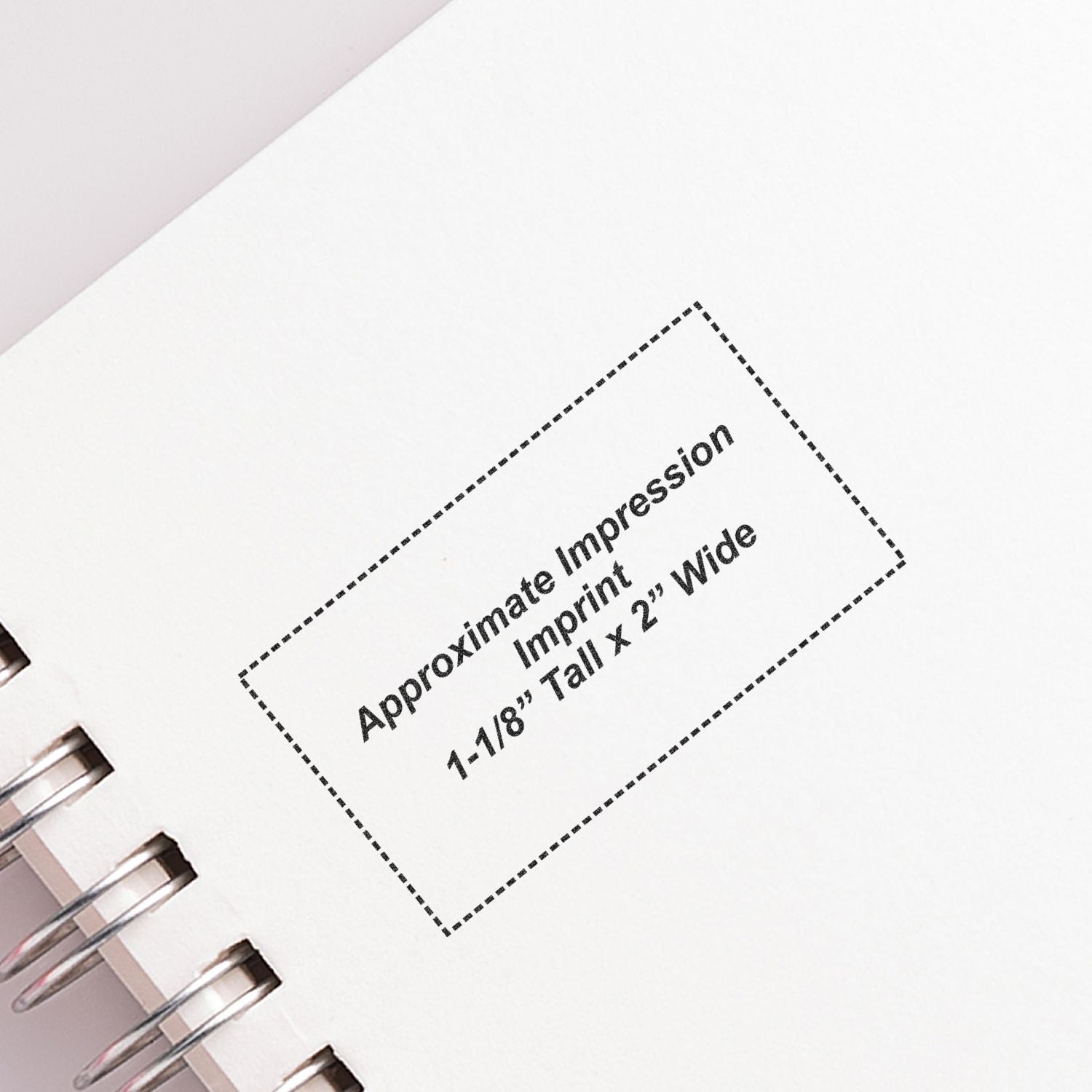 Close-up of spiral notebook page showing approximate impression imprint size guide, 1-1/8" tall x 2" wide for custom printing.