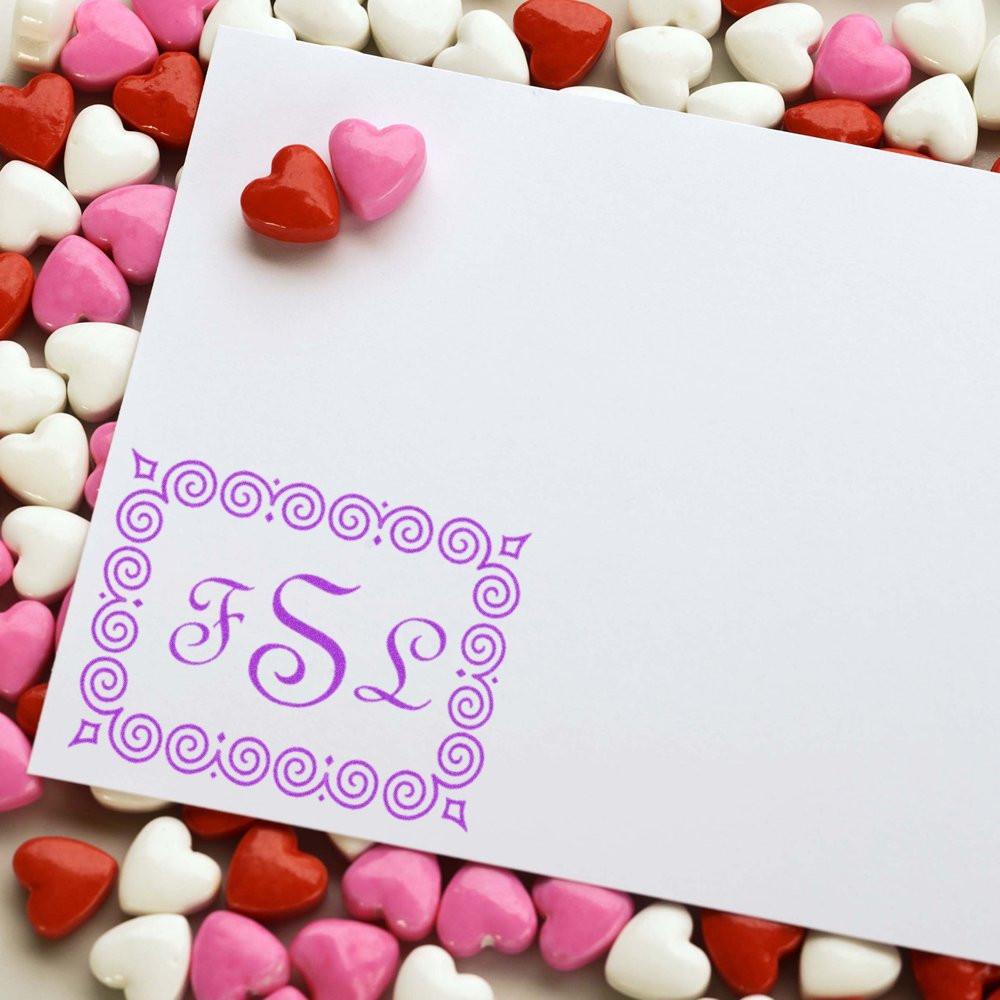 Custom monogram rubber stamp on a blank card, framed by heart candies for Valentines Day crafts.
