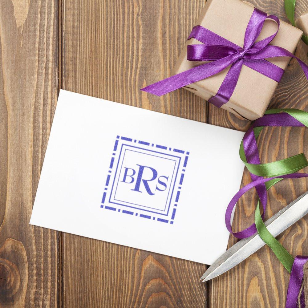 Custom rubber stamp monogram imprint on gift card beside ribbon-wrapped present on rustic wood table