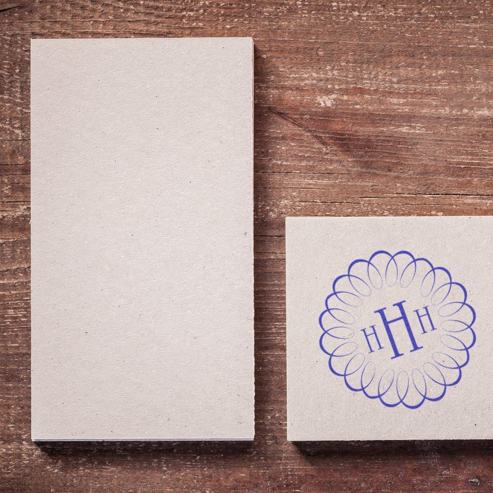 Custom rubber stamp monogram on cardstock next to blank card, ideal for branding, invitations, and packaging.