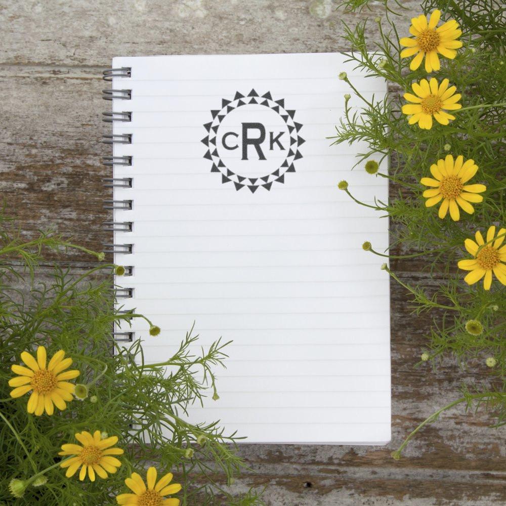 Custom monogram rubber stamp on spiral notebook with decorative circle logo and yellow flowers for personalized stationery.