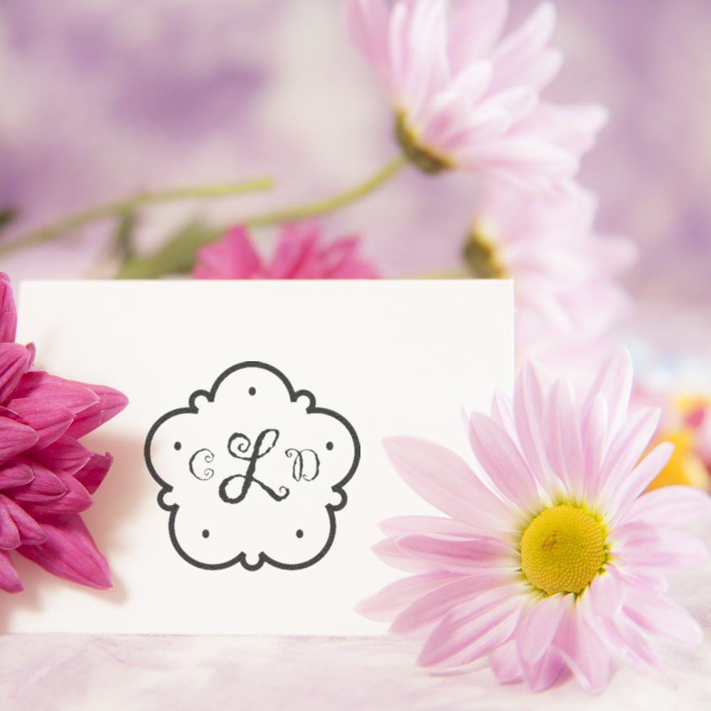 Personalized floral monogram rubber stamp with ornate initials, styled on a card with pink flowers.