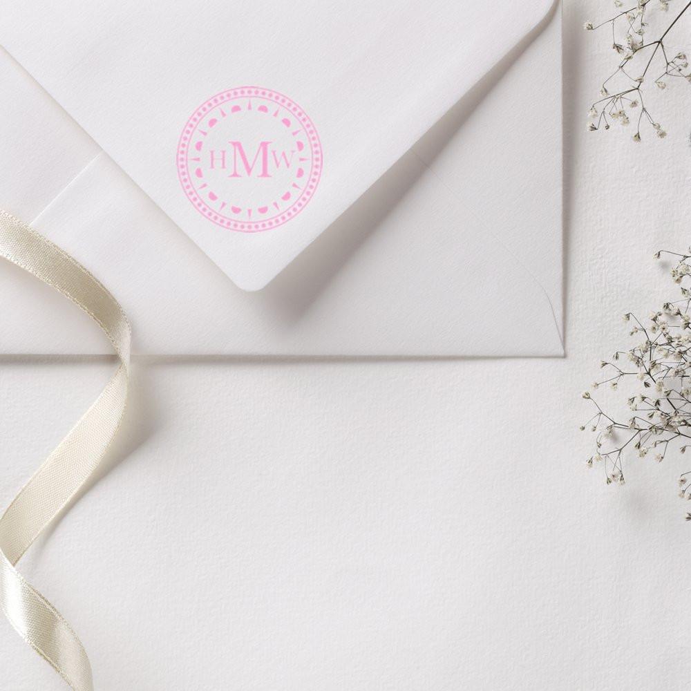 Custom pink monogram rubber stamp on a white wedding invitation envelope with ribbon and floral accents