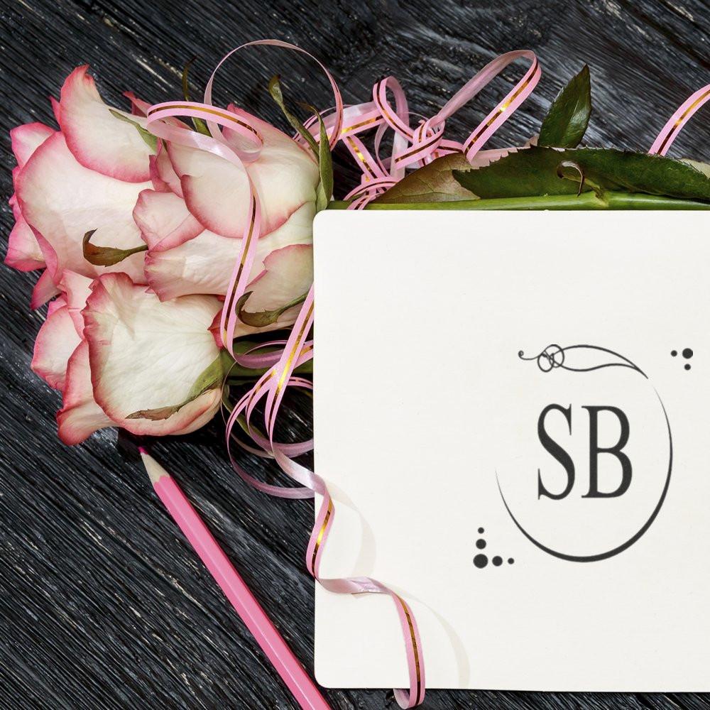 Custom monogram rubber stamp impression on a wedding-style card with pink roses and ribbon for personalized stationery.