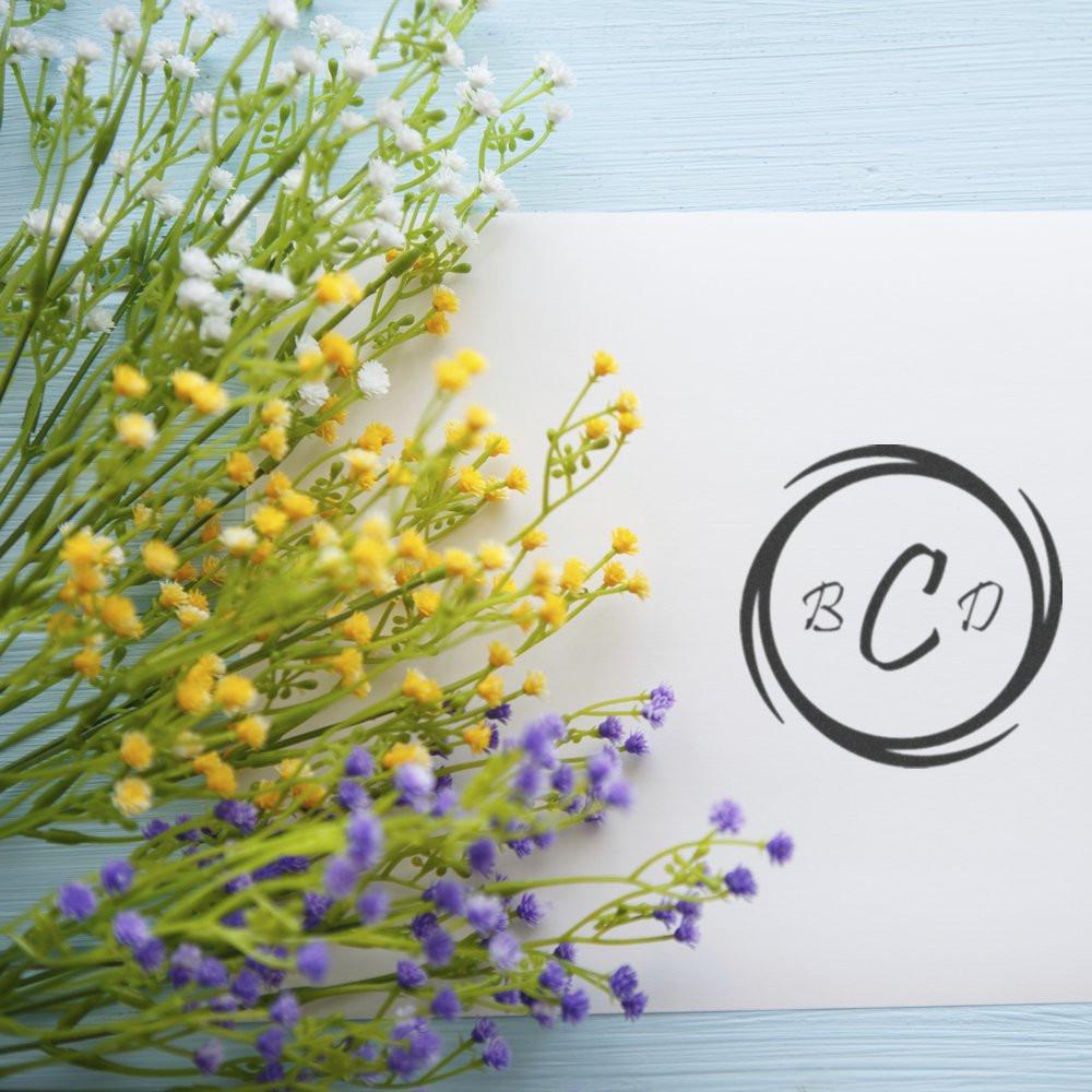 Custom rubber stamp with BCD monogram logo beside colorful floral arrangement on a white card.