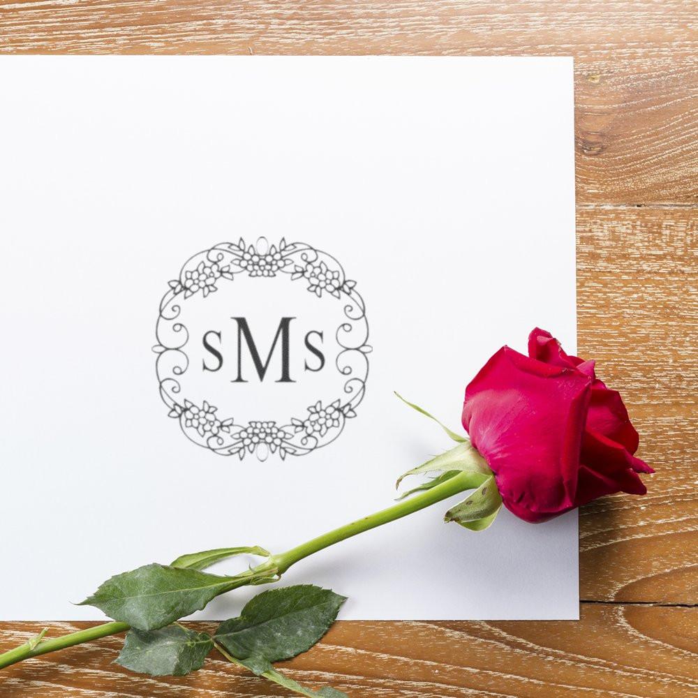 Custom floral monogram rubber stamp with sMs on white paper, styled with a pink rose on a wood table.