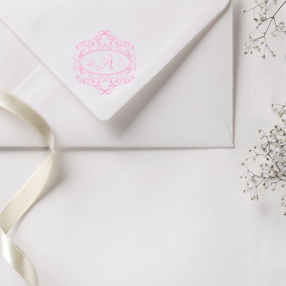 Custom pink monogram rubber stamp on a white wedding envelope for personalized invitations and stationery.