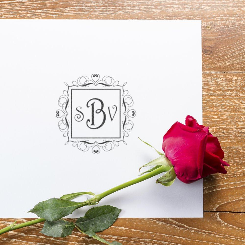 Ornate custom monogram rubber stamp design with floral frame on white paper and red rose