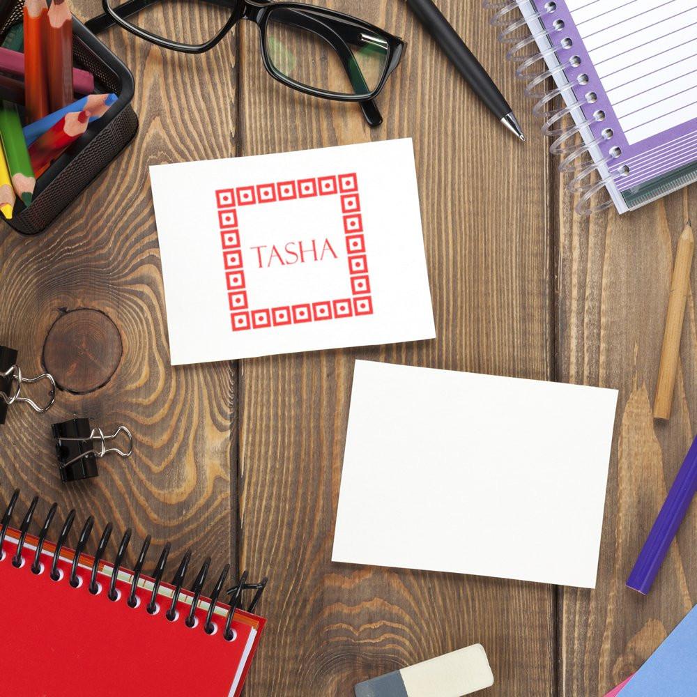 Custom rubber stamp with personalized name design on stationery, shown on a desk beside a blank card and office supplies.