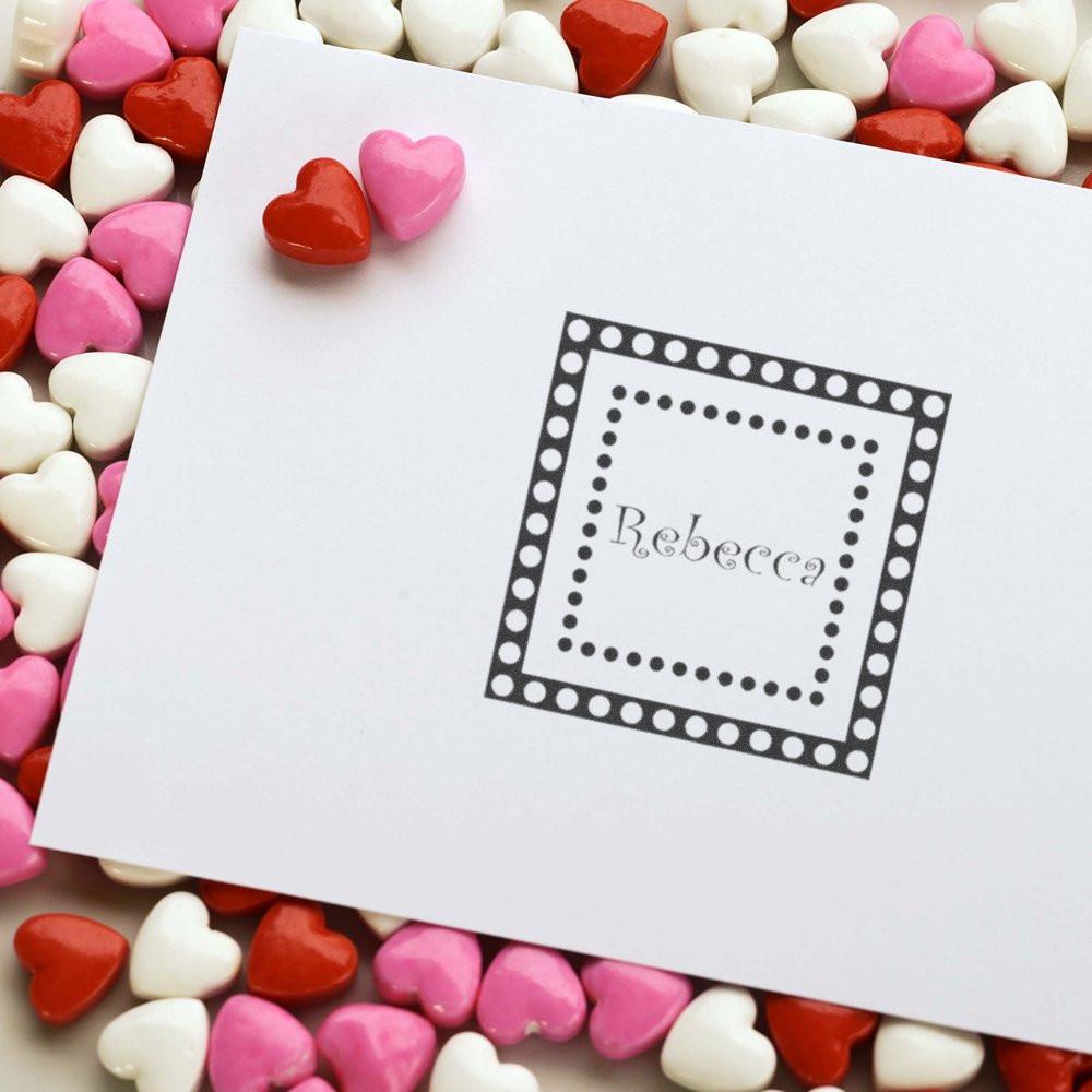 Personalized rubber stamp with name Rebecca and dotted square border on a card, surrounded by heart candies.