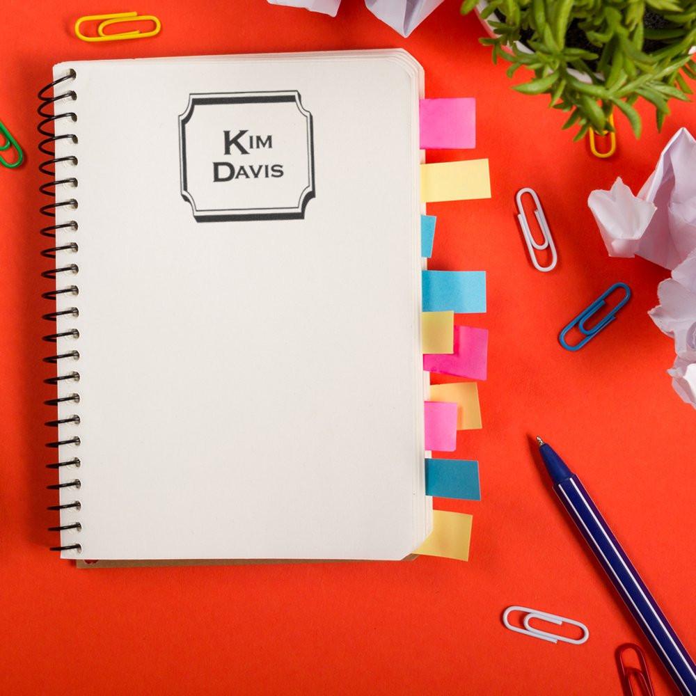 Custom rubber name stamp on a notebook cover with sticky tabs, ideal for personalized office branding and stationery.