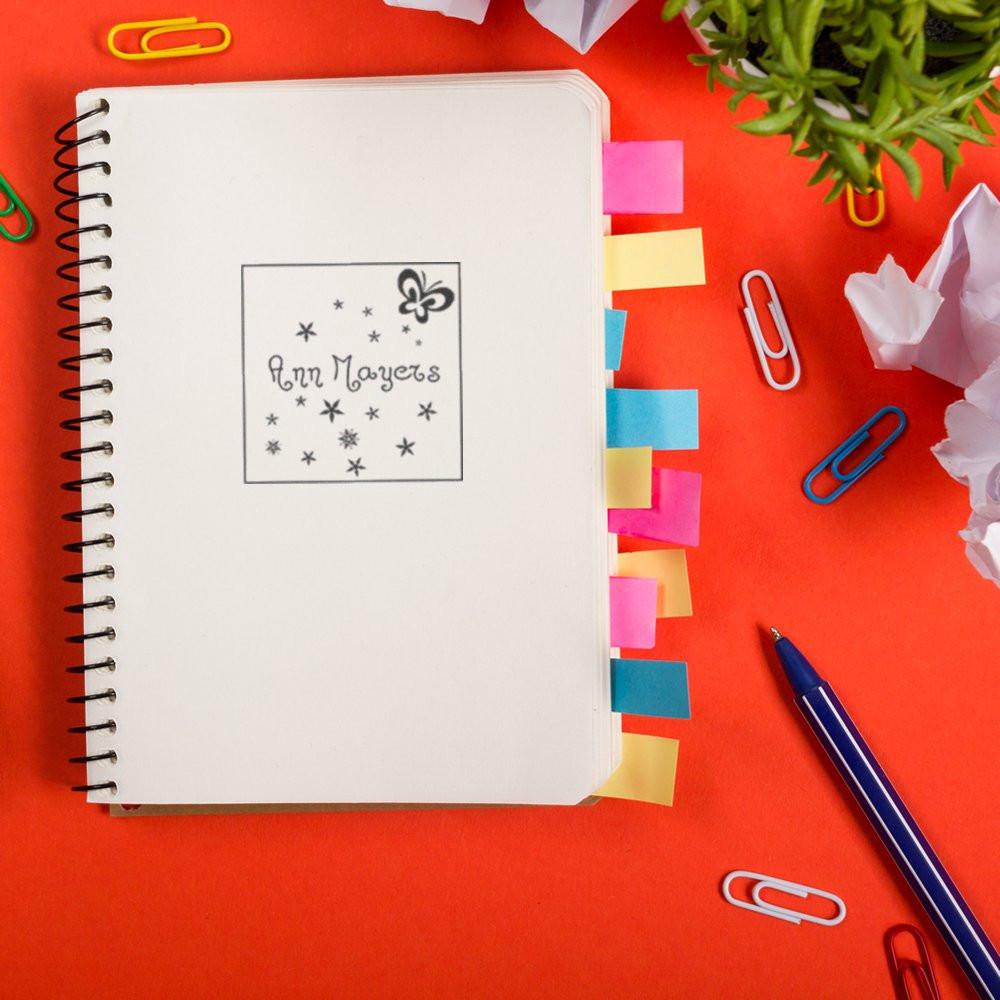 Custom name rubber stamp with butterfly design on a notebook, ideal for personalized stationery and branding.