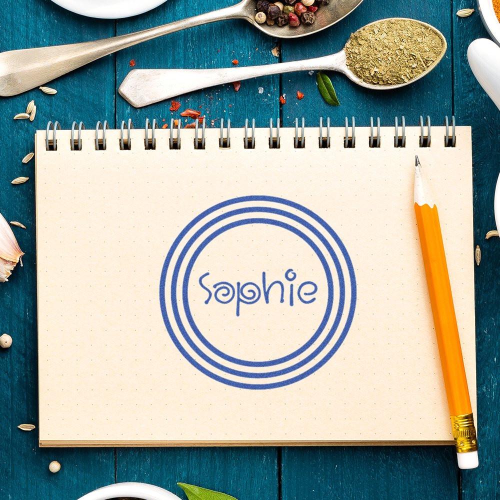 Custom logo rubber stamp with the name Sophie, shown as a blue circular imprint in a notebook.