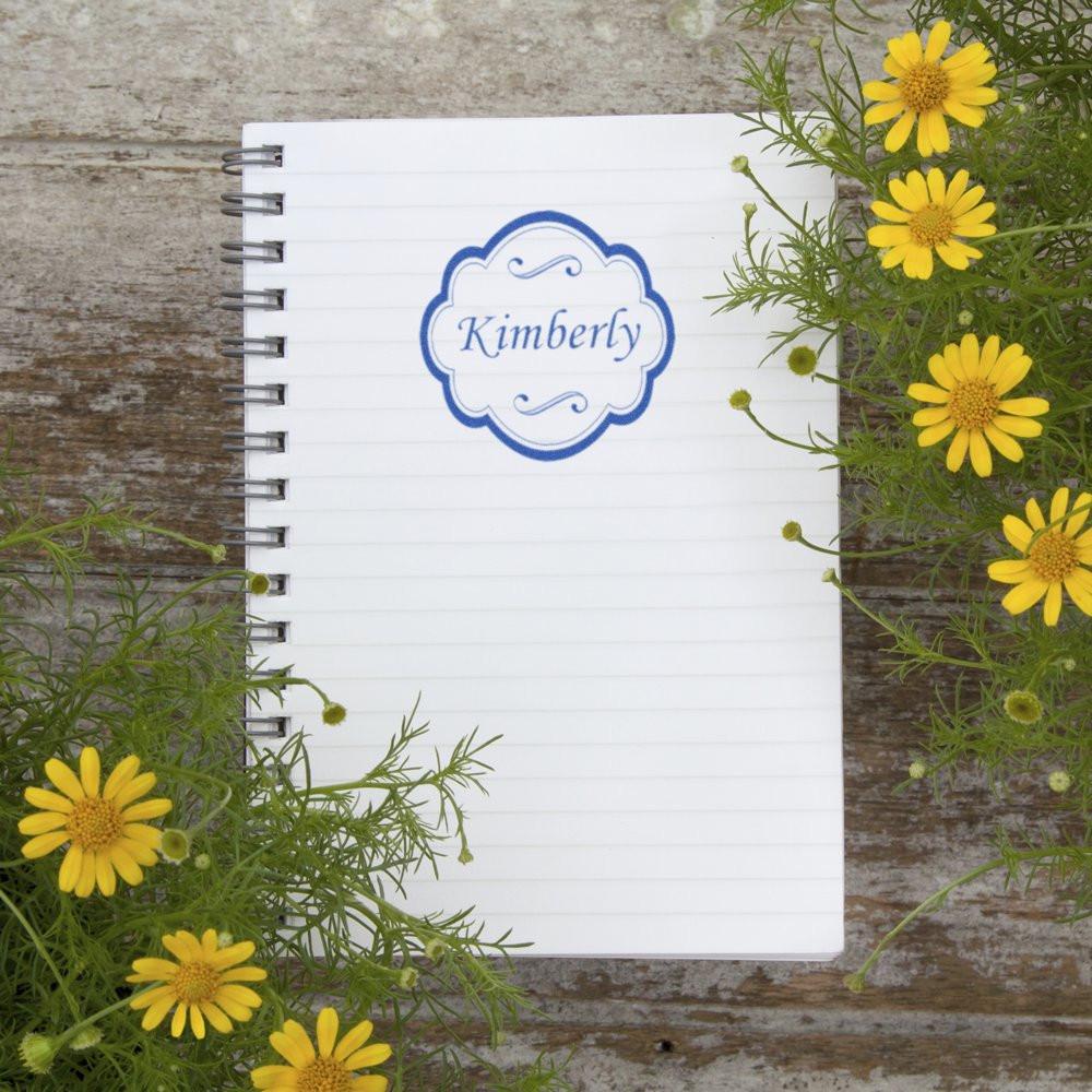 Personalized Kimberly rubber stamp in a blue decorative frame on a notebook, ideal for custom stationery and branding.