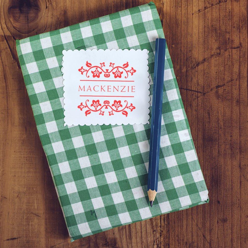 Custom personalized rubber stamp impression with floral Mackenzie name design on a green gingham notebook