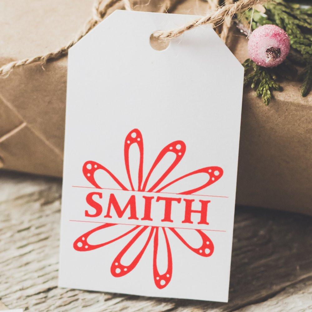 Personalized red rubber name stamp reading SMITH on a white gift tag for custom packaging and holiday gifting.