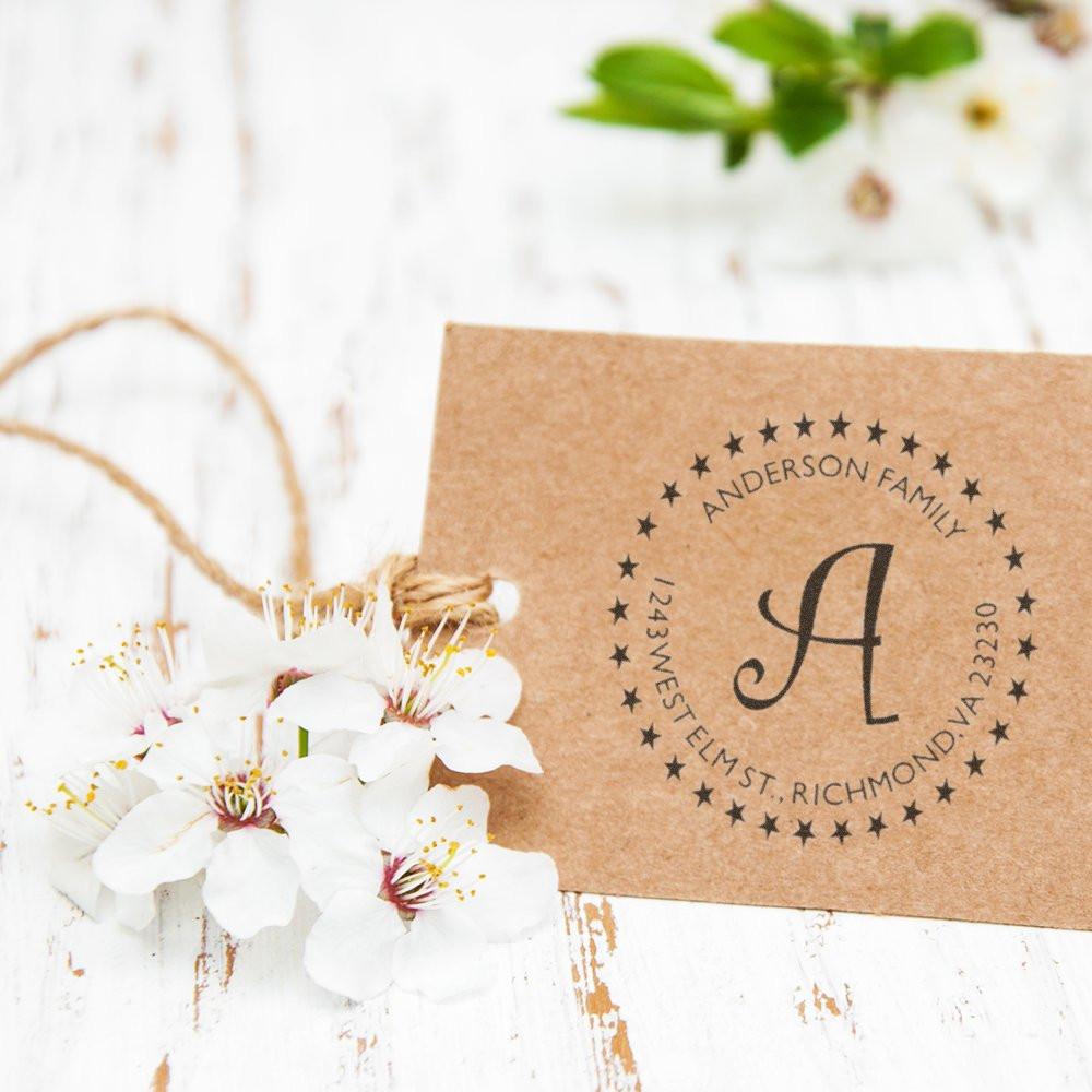 Kraft Anderson Family monogram gift tag with address and twine, next to white flowers on rustic backdrop for wedding or home decor.